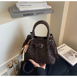 Detail of leopard print bucket bag featuring brown leather handle and colorful bead tassel
