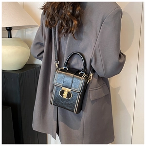 Detail of black crossbody bag featuring gold T-clasp and elegant contrast stitching