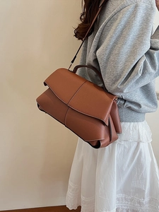Brown leather crossbody bag with white stitching shown on a model in a minimalist style