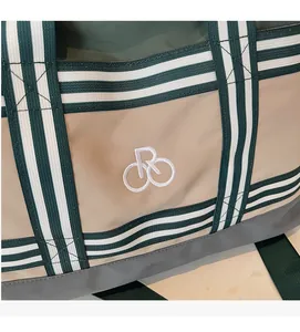 Gros plan sur la texture en toile kaki et la sangle rayée verte du sac de sport