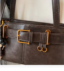 Close-up of vintage dark brown leather bag with golden buckle and wooden bead charm