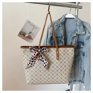 Détail du cabas monogramme beige avec nœud léopard sur un cintre avec du denim