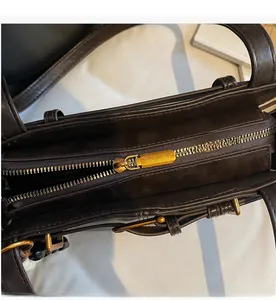 Detailed close-up of the smooth golden metal zipper and stitching on the dark brown handbag