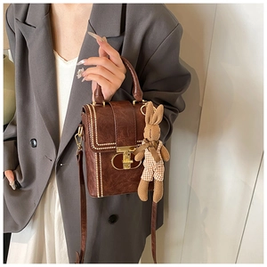 Detailed side view of a brown vintage mini bag with pearl-dotted trim and plush rabbit charm