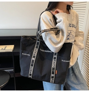 Detail der schwarzen Nylon-Tasche mit gemustertem Jacquard-Gurt und orangem Etikett