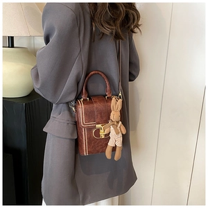 Detail of vintage brown leather crossbody bag with rabbit charm and decorative white stitching