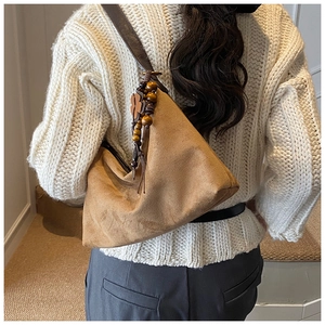Detail of camel suede hobo bag featuring decorative wood bead tassels and clover charm