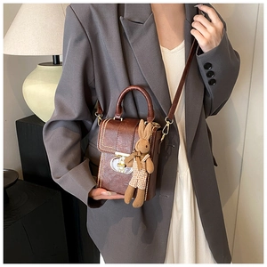 Detail view of brown PU leather crossbody bag with metal clasp and plaid bunny charm
