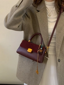 Vintage burgundy leather crossbody bag with gold buckle on a model in wool coat