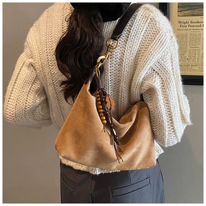 Detail view of brown suede hobo bag with vintage metal clasp and ethnic tassel decoration