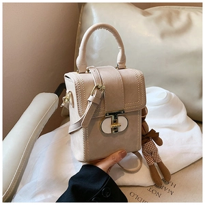 Detail of beige pebbled leather handbag with gold T-clasp and cute bear charm