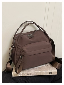 Detail of a dark brown nylon handbag with metal snap button and broad shoulder strap