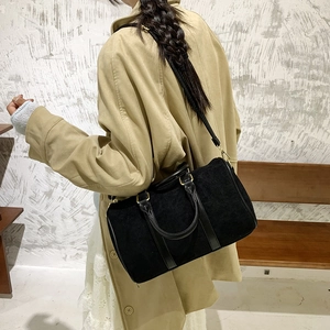 Detail view of black frosted suede Boston bag with golden metal buckles on a camel coat