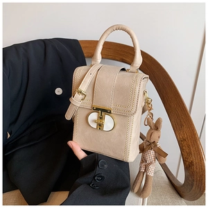 Detail of small beige structured handbag with gold hardware and plush bunny charm