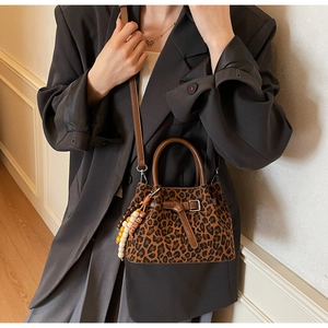 Close-up of leopard print bucket bag featuring brown leather handles and beaded tassel detail