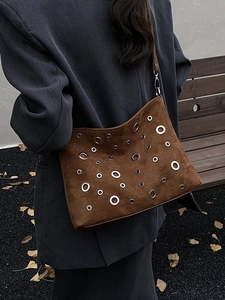 Sac bandoulière en daim marron avec œillets argentés porté sur un manteau gris
