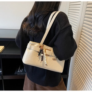 Detail of minimalist cream shoulder bag featuring decorative strap and wooden bead charm