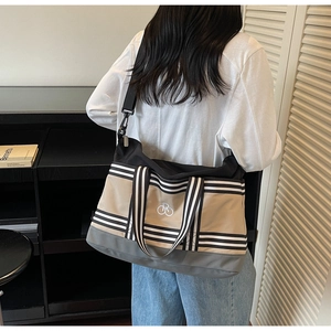 Détail d'un grand sac fourre-tout en toile kaki avec poignées rayées et bandoulière noire