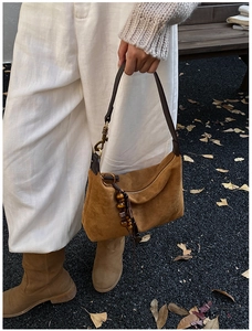 Close-up of brown suede hobo bag with wooden bead tassel and brass hardware outdoors
