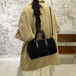 Detail of a black cylinder bag featuring matte finish and gold hardware on a stylish model