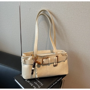 Detail of cream shoulder bag featuring vintage gold buckle and bead charm accessory