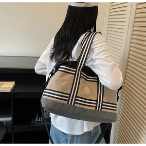 Détail d'un grand sac de voyage bicolore en toile avec bandoulière rayée porté par mannequin