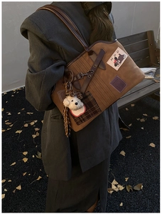 Detail view of large brown suede tote bag with cartoon puppy embroidery and plush charm
