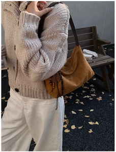 Detail of caramel suede hobo bag with wooden bead charm in a natural autumn outdoor setting