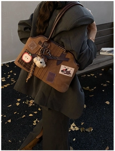 Close-up of brown canvas tote bag with apple embroidery, dog patch and plush bear charm