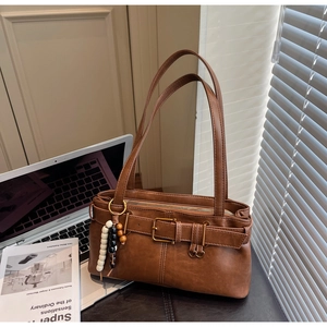 Detail of a brown leather shoulder bag with buckle belt and beaded charm on a workspace