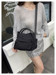 Detail of a black nylon crossbody bag with multi-pocket design shown on a street model