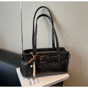 Detail of black faux leather bag with buckle strap and decorative beaded pendant on books