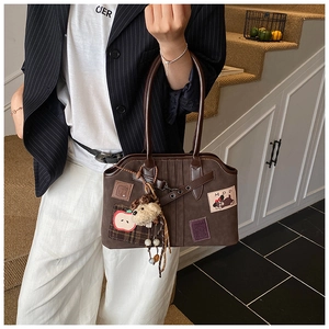 Close-up of brown tote bag featuring apple embroidery and plush pendant detail