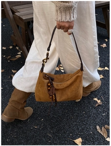 Close-up of brown suede hobo bag with fringe and leaf charms on autumn street background