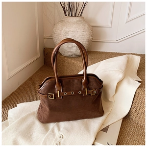 Detail of dark brown suede tote bag featuring leather handles and gold metal hardware