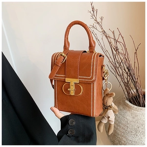 Detail of a brown vintage-style mini square bag with a golden T-lock and rabbit charm