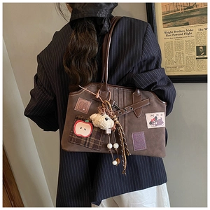 Close-up detail of vintage brown tote bag with apple embroidery and plush doll charm