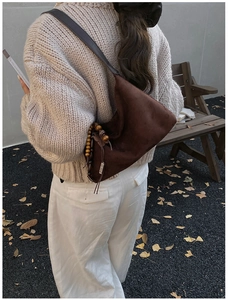 Detail of dark brown faux suede crescent bag with ethnic beaded leaf pendant on a shoulder strap