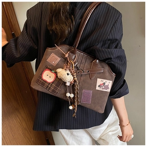 Detail of a brown tote bag with cute apple embroidery and a plush bear charm on shoulder