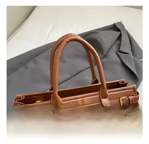 Detail of brown leather tote with triangular metal logo and side belt buckle straps