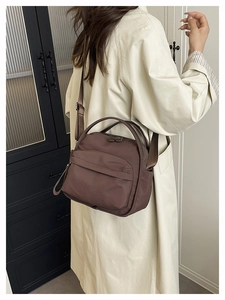 Deep brown nylon crossbody bag worn by a model in a minimalist indoor casual lifestyle setting