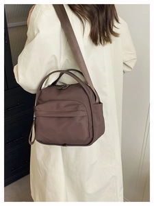Detailed view of a dark brown nylon crossbody bag worn by a model in a casual indoor setting
