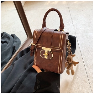 Close-up of retro brown leather phone bag featuring gold rivets and a plush bear charm
