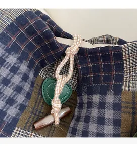 Detail of plaid tote bag featuring rope closure, toggle button, and green heart leather patch
