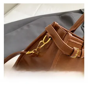 Detail of golden metal hook and brown pebbled leather strap on a small crossbody bag