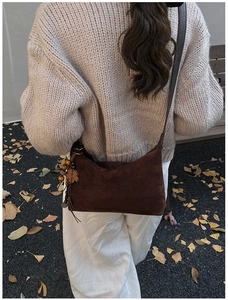 Detail view of brown suede underarm bag with decorative wooden beads and clover charm