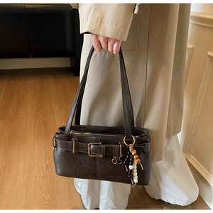 Close-up of a vintage dark brown shoulder bag with a belt buckle and wooden bead charm