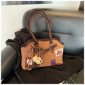 Detail of brown suede tote bag with apple embroidery, plaid patches and plush dog charm