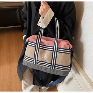 Détail du sac de voyage tricolore avec poignées rayées et logo brodé blanc