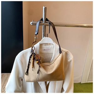 Detail of khaki suede hobo bag with dark leather strap and clover bead charm on a blazer